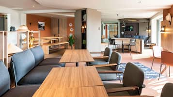 A modern hotel lobby with seating areas, a reception desk, and a kitchen in the background.
