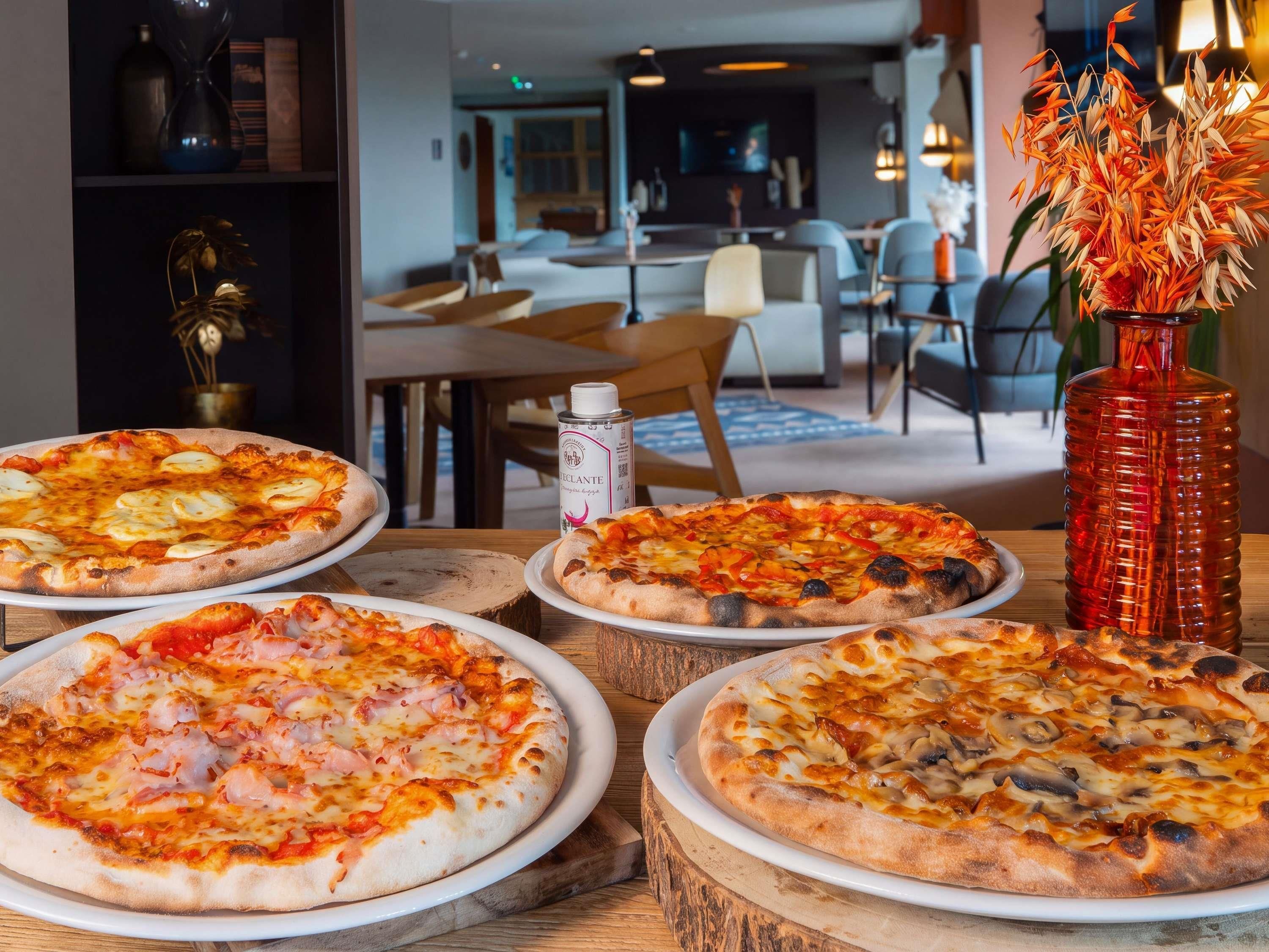 A dining area with multiple pizzas on wooden boards, a vase with flowers, and a can of sauce.