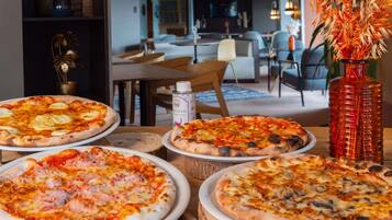 A dining area with multiple pizzas on wooden boards, a vase with flowers, and a can of sauce.