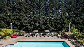 A pool area with lounge chairs and umbrellas, surrounded by trees.