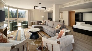 Una habitación de hotel moderna con una cama grande, un sofá, una zona de comedor y un balcón con vistas.