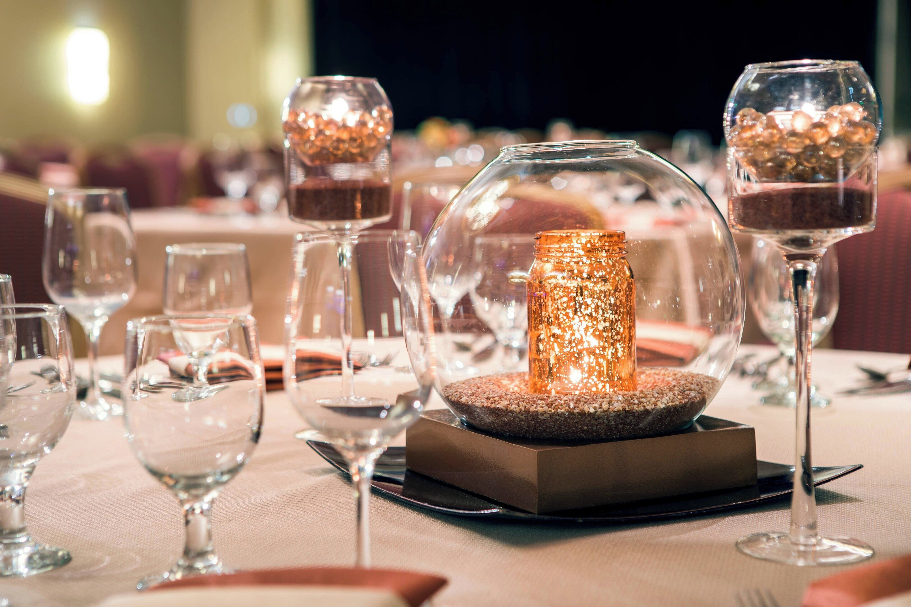A table set with clear wine glasses, a central decorative candle, and a square base.