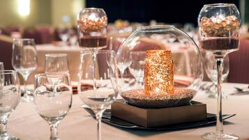 A table set with clear wine glasses, a central decorative candle, and a square base.