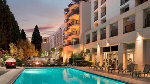 Un hotel moderno con piscina, asientos al aire libre y balcones.