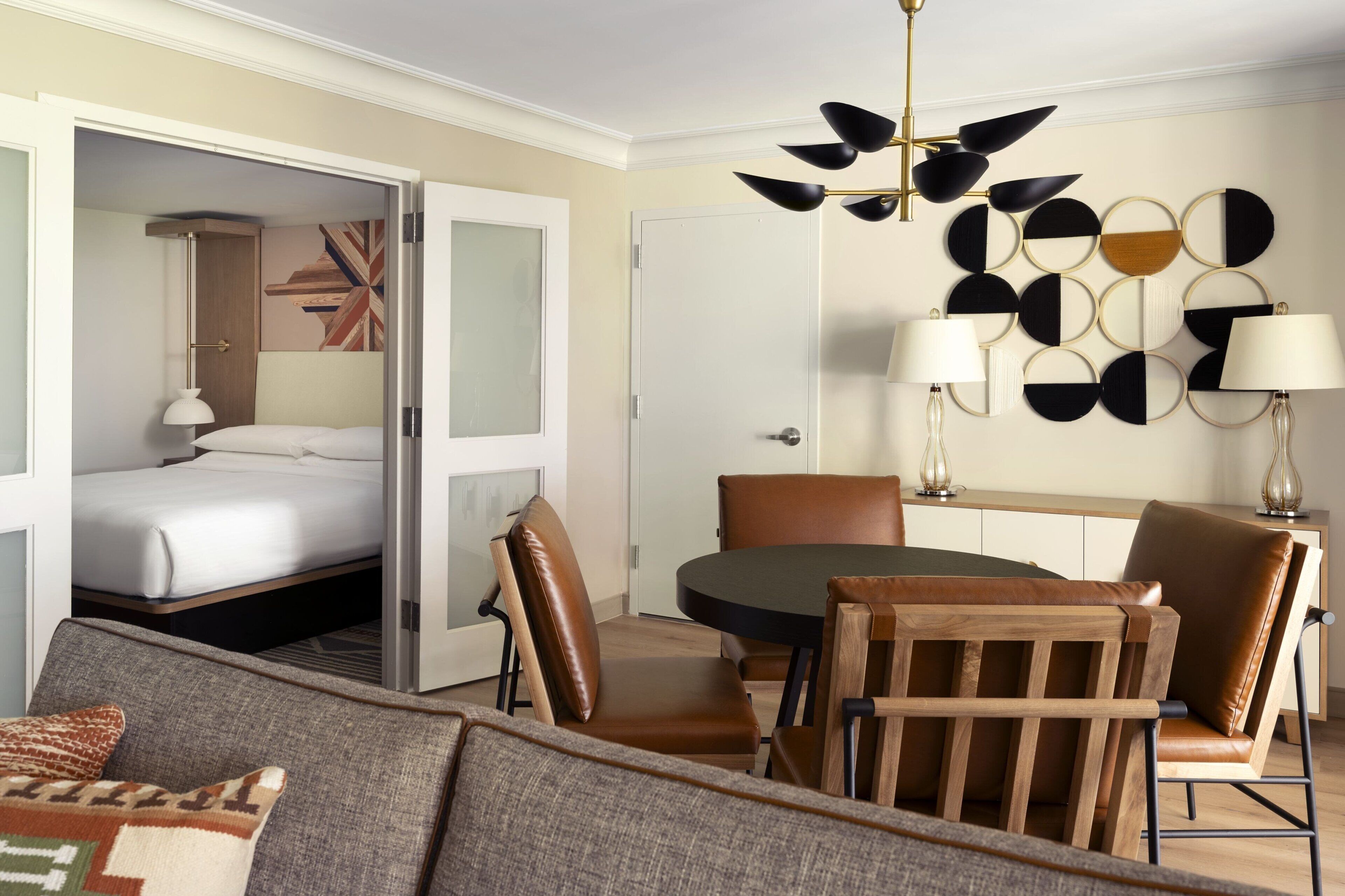 A hotel room with a bed, a dining table with chairs, a sofa, and a decorative wall piece.