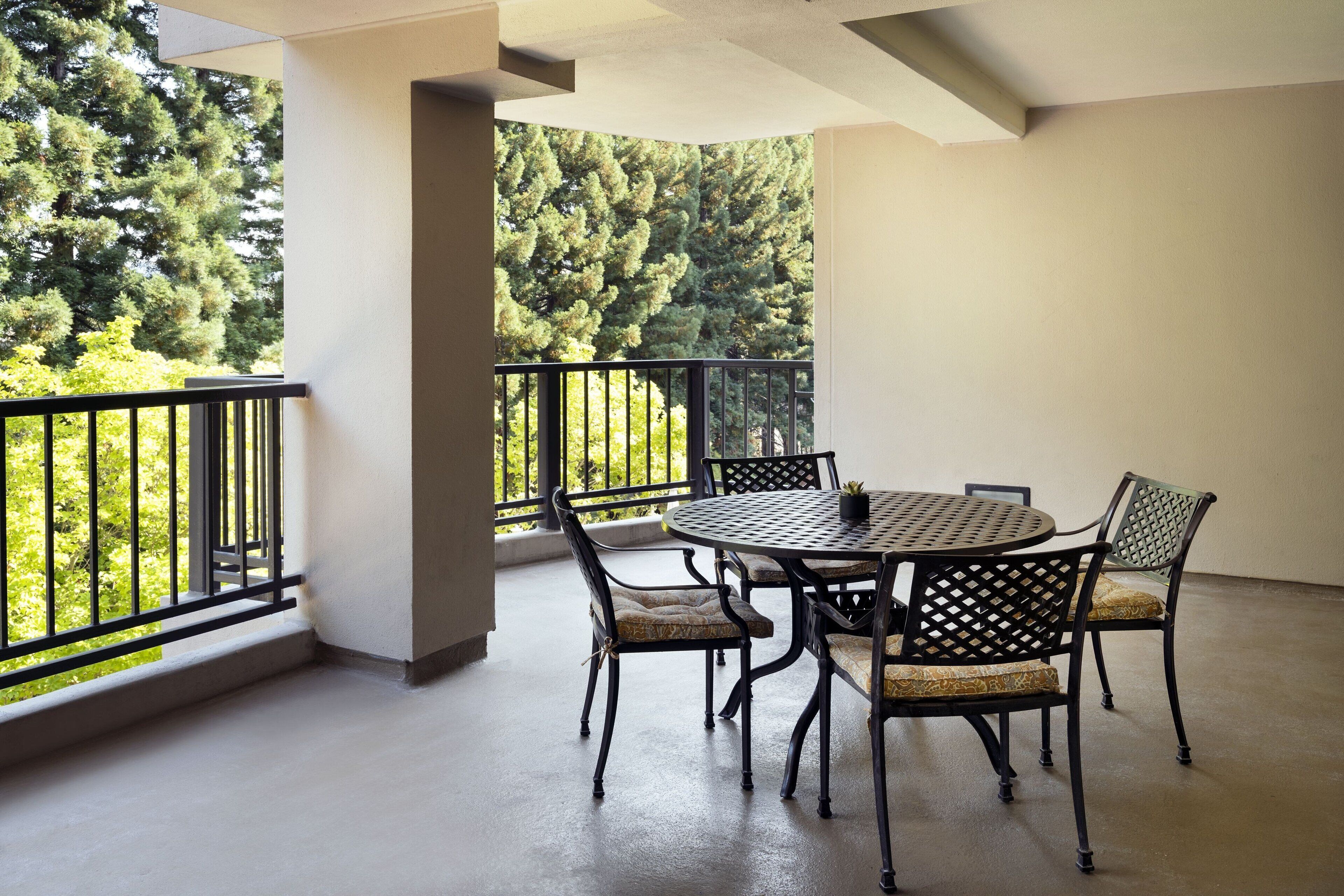 A balcony with a round table and chairs, surrounded by a black metal railing.