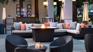Un área de estar al aire libre con una mesa de fuego, muebles de mimbre y una barra con botellas.