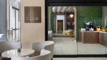 Ein moderner Lounge-Bereich mit einem 'CLUB'-Schild, bequemen Sitzgelegenheiten und einem Blick auf eine Küchenzeile mit einer Kaffeemaschine.