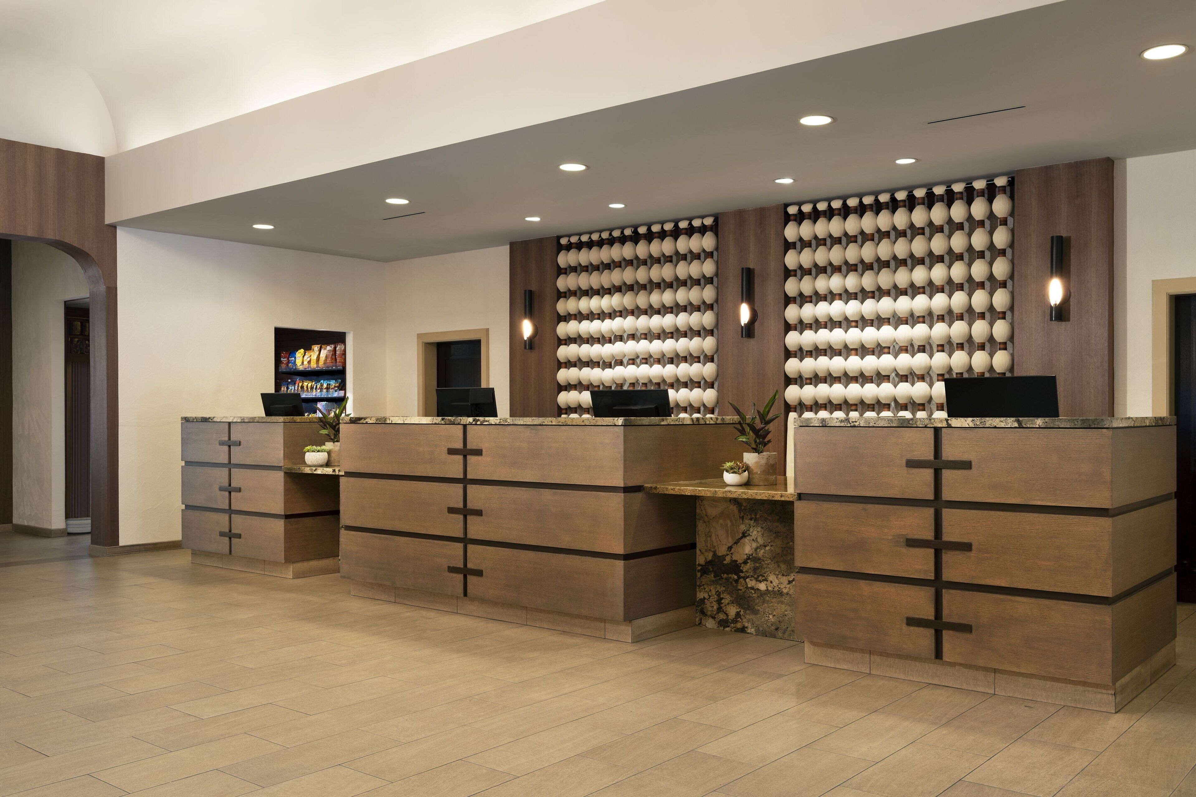 A reception area with a modern design, featuring a central counter with a digital screen, a wall-mounted display, and a decorative wall with spherical elements.