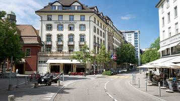 Un hotel de estilo arquitectónico europeo clásico, que presenta una entrada destacada con un balcón y una bandera.