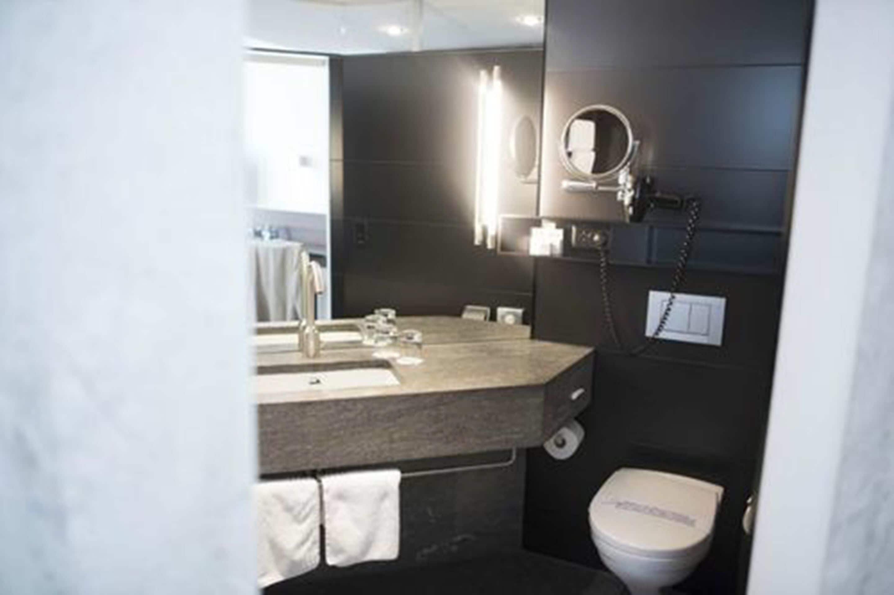 Een moderne badkamer met een donkere muur, een wastafel met spiegel, toilet en een handdoekrek.