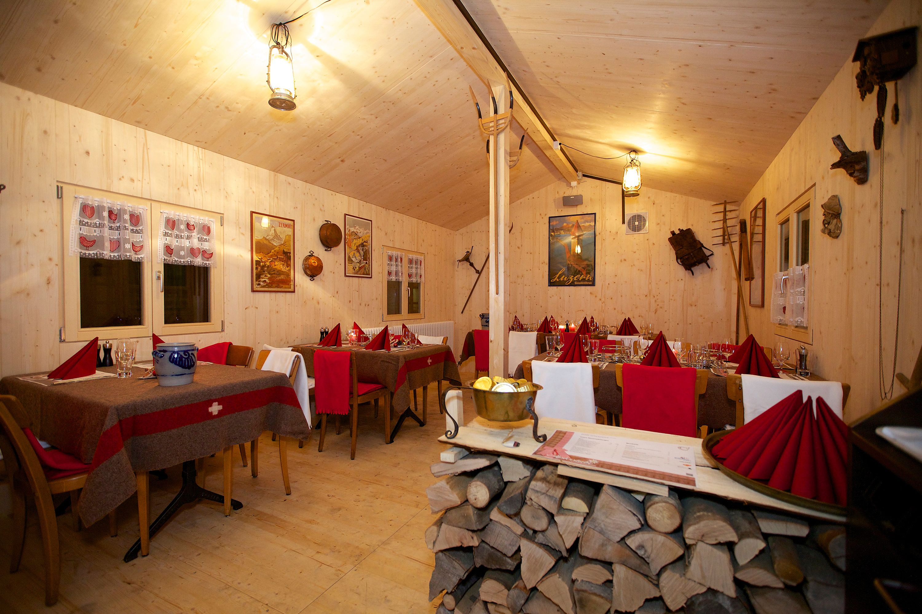 A wooden interior with tables set for dining, wooden walls, and a stack of firewood.