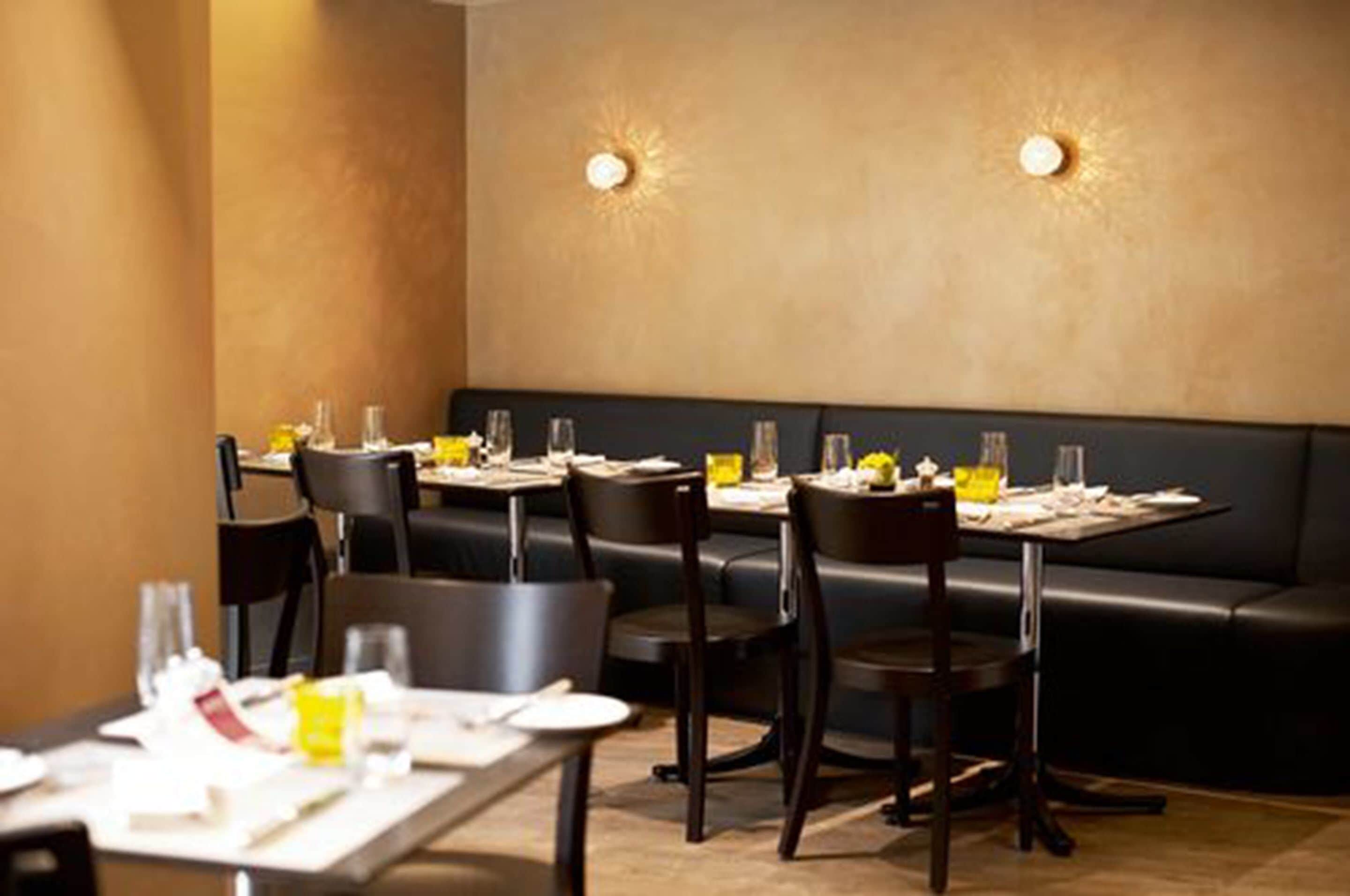 A restaurant with tables set for dining, black leather booths, and wall-mounted lighting.