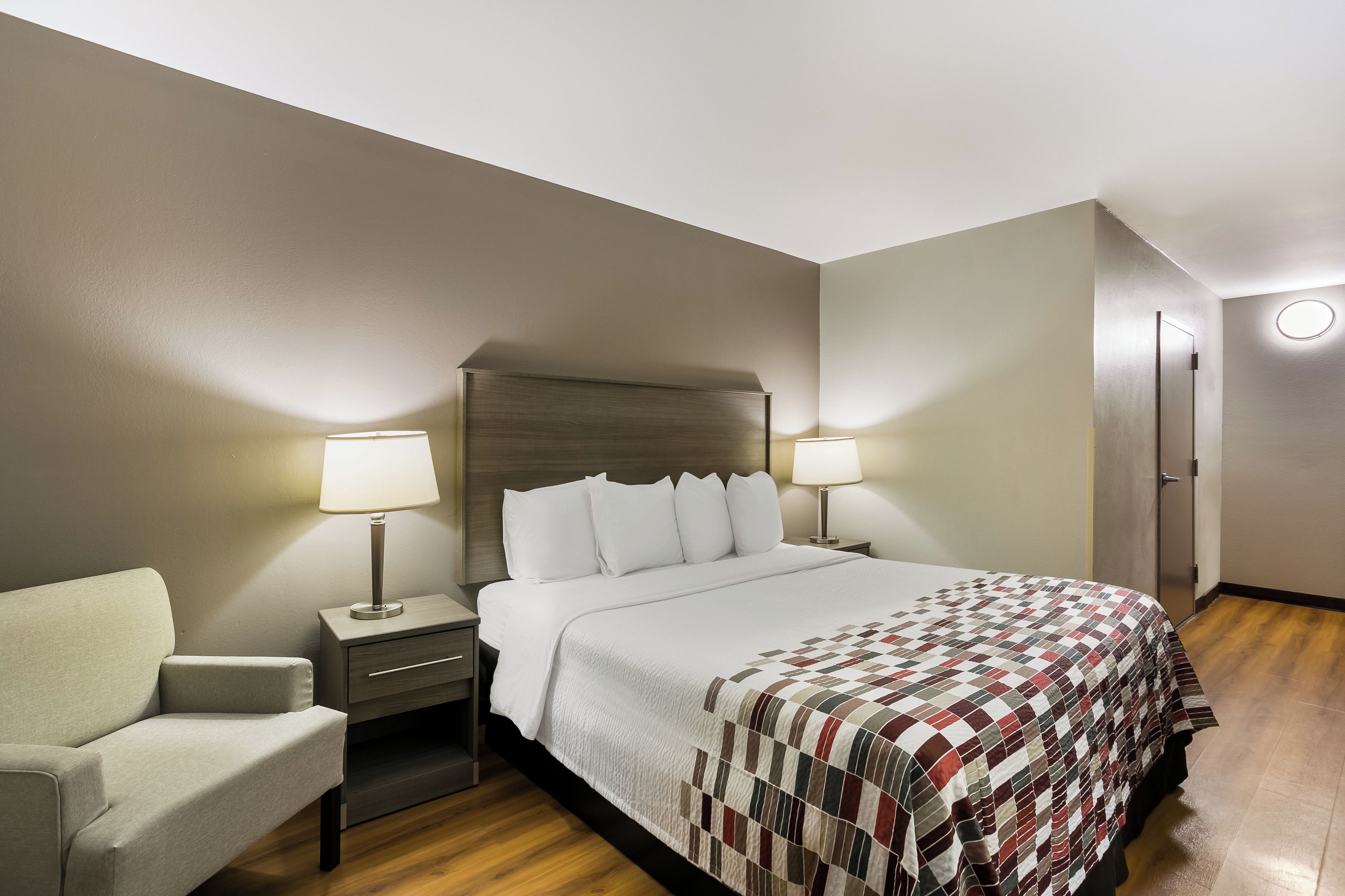 A hotel room with a bed, two bedside tables, a chair, a wardrobe, and a round light fixture on the wall.