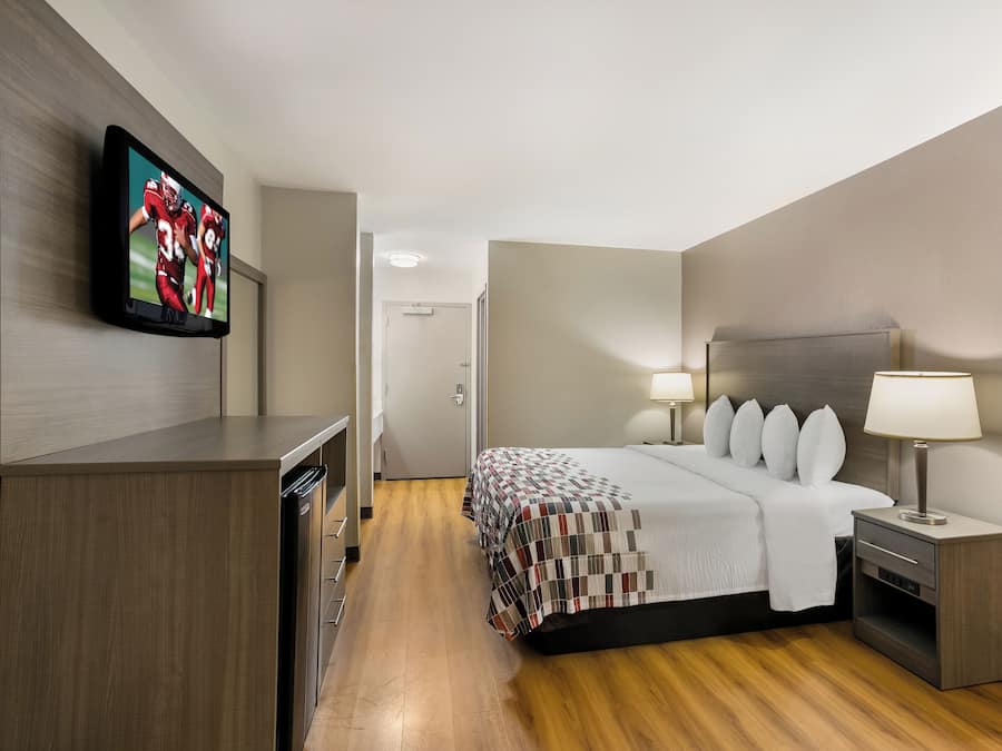 A hotel room with a bed, bedside tables, a TV mounted on the wall, and a wooden floor.