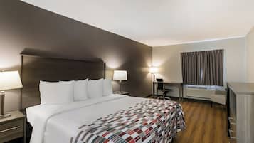 Habitación de hotel con una cama grande, dos mesitas de noche con lámparas, un escritorio con silla, una ventana con cortinas y un equipo de aire acondicionado integrado.