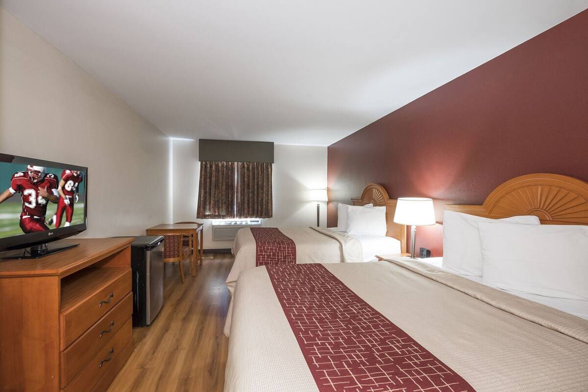 A hotel room with a bed, bedside table, lamp, TV, and a desk with a chair.