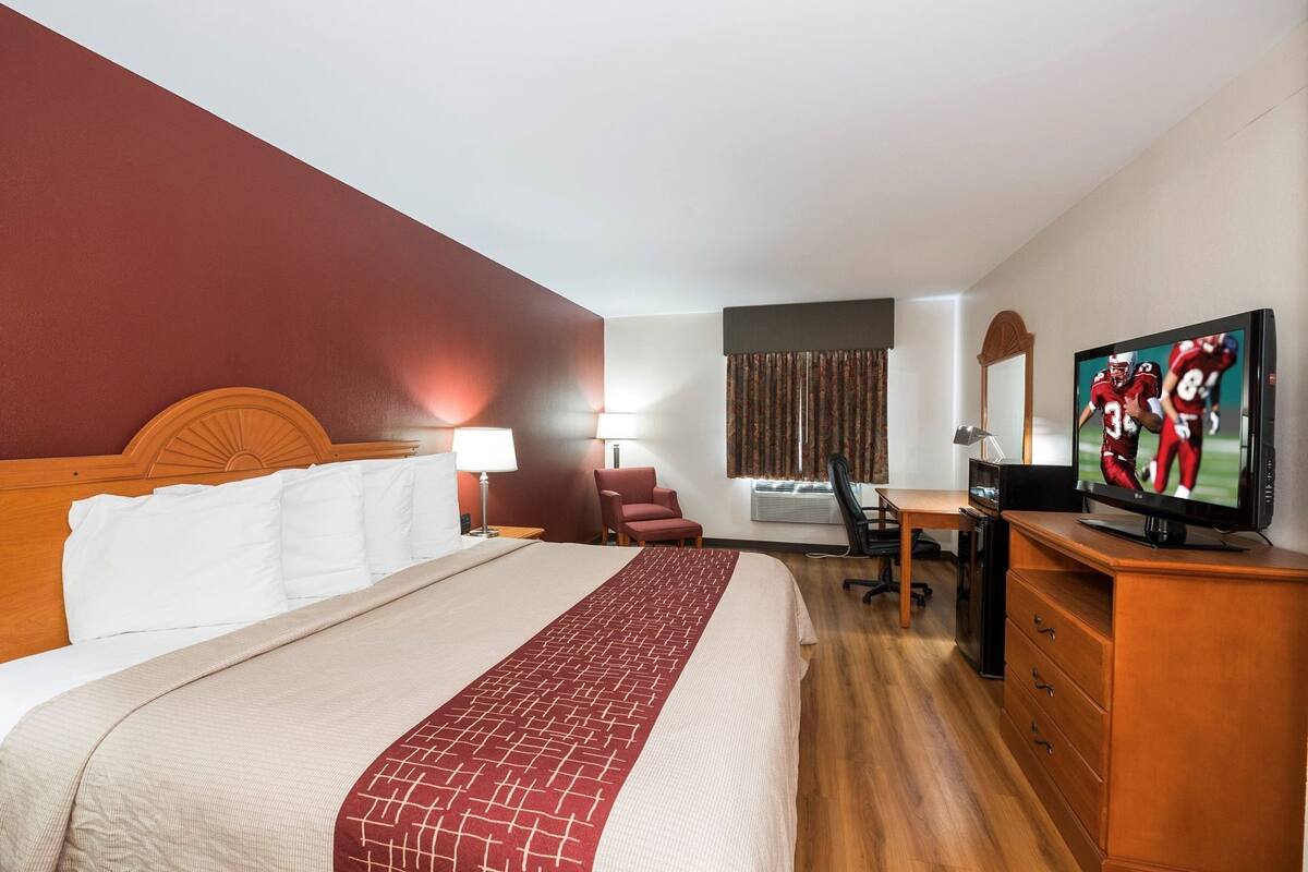 A hotel room with a bed, desk, chair, TV, and a window with curtains.