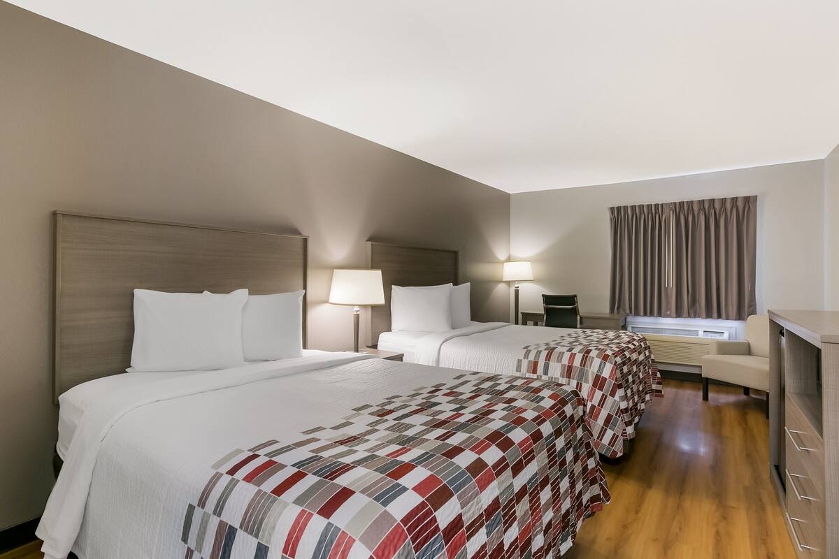 A hotel room with two beds, a desk, a chair, and a window with curtains.
