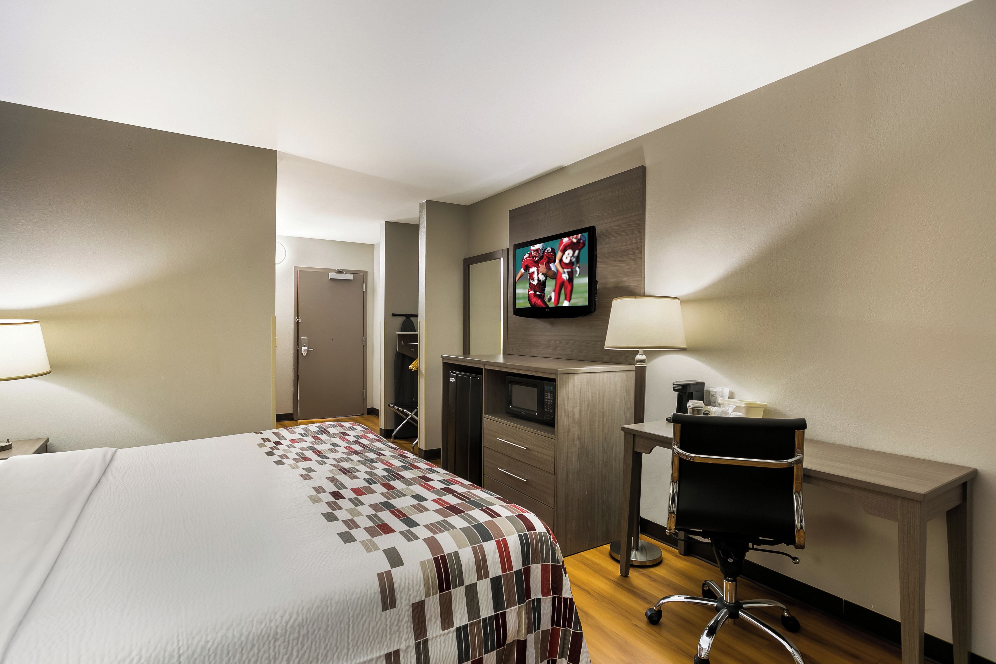A hotel room with a bed, a desk, a television, and a chair.