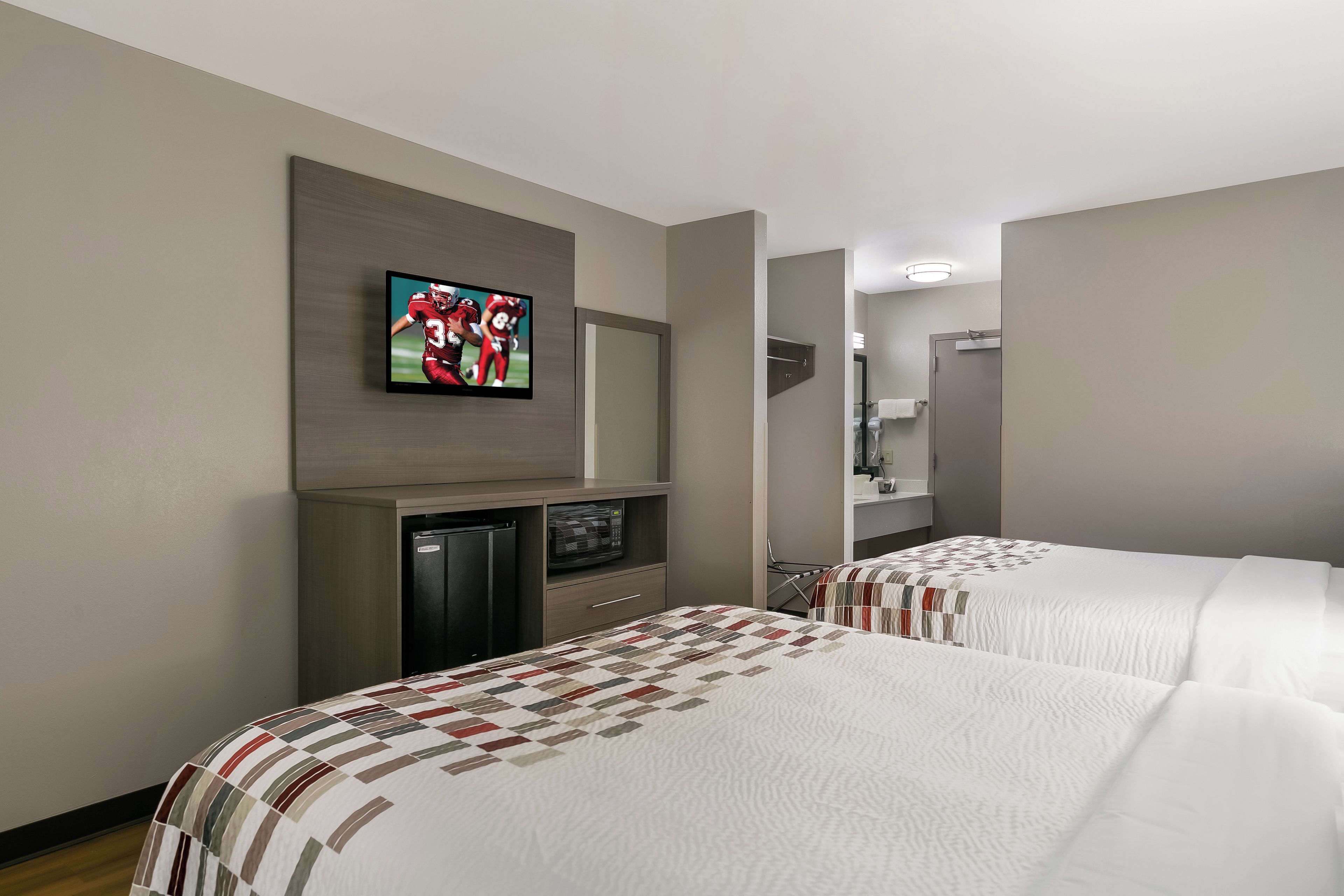 Habitación de hotel con dos camas, un televisor montado en la pared, microondas y refrigerador.