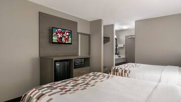 A hotel room with two beds, a television mounted on the wall, a microwave, and a refrigerator.