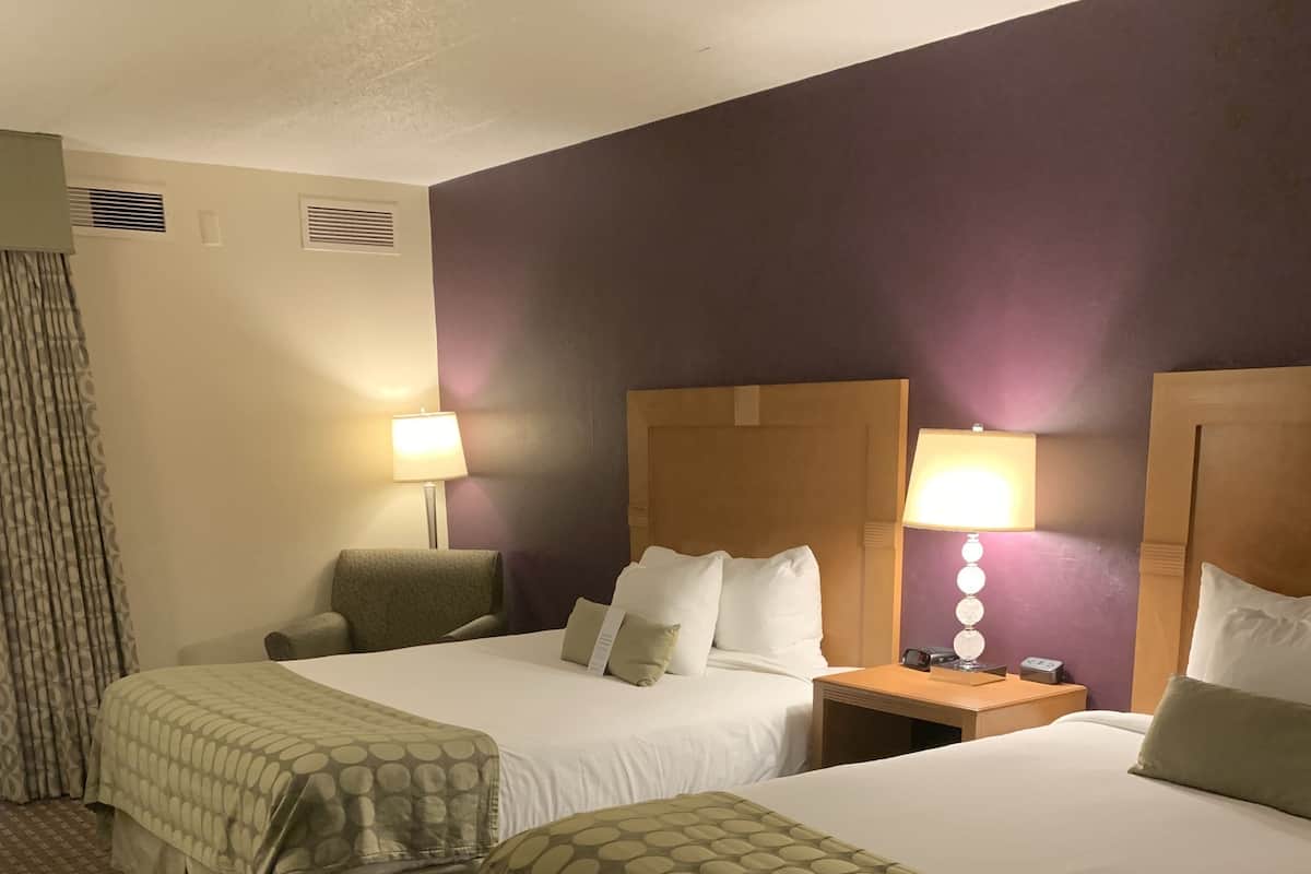 A hotel room with two beds, a nightstand, a lamp, and a chair.