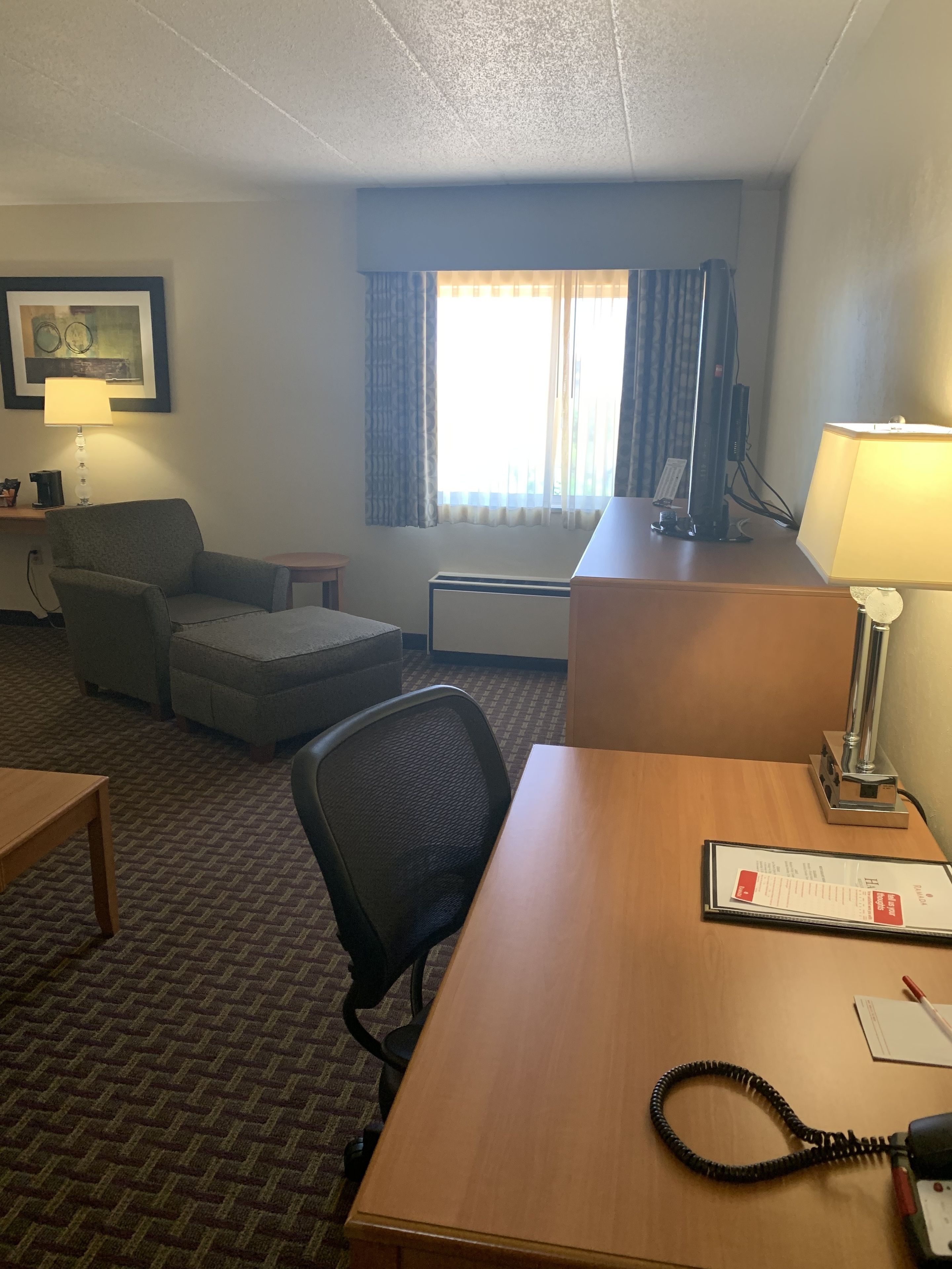 Une chambre d’hôtel équipée d’un bureau, d’une chaise, d’un canapé, d’une lampe, d’un ordinateur et d’une fenêtre avec des rideaux.