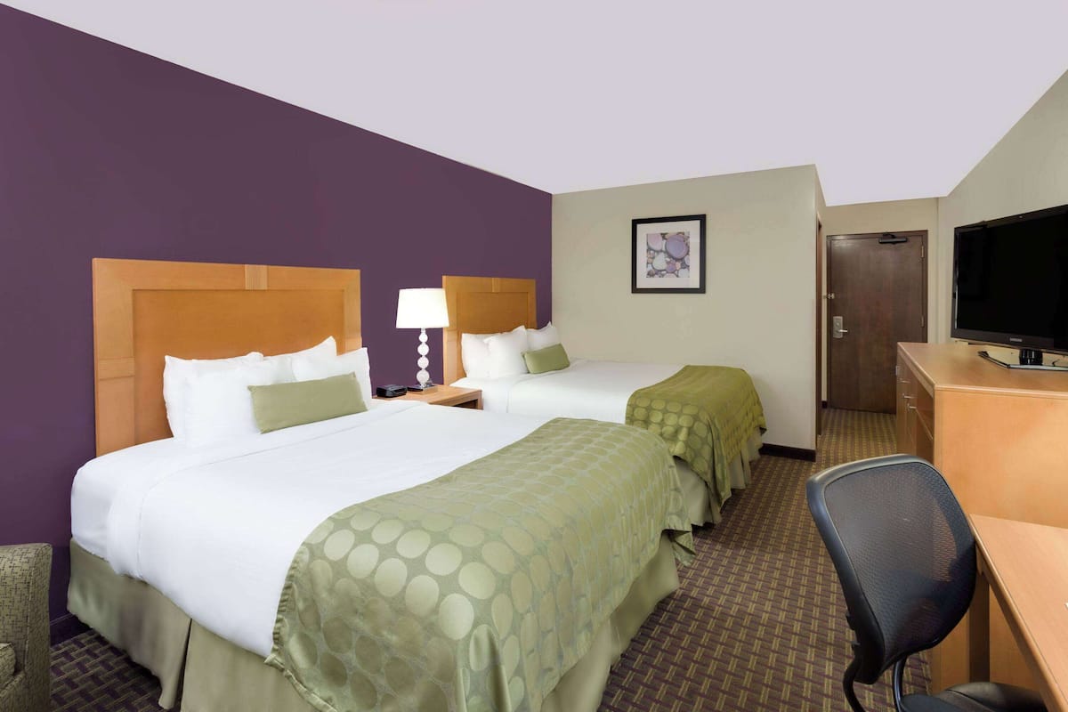 A hotel room with two beds, a desk, a chair, a television, and a door.