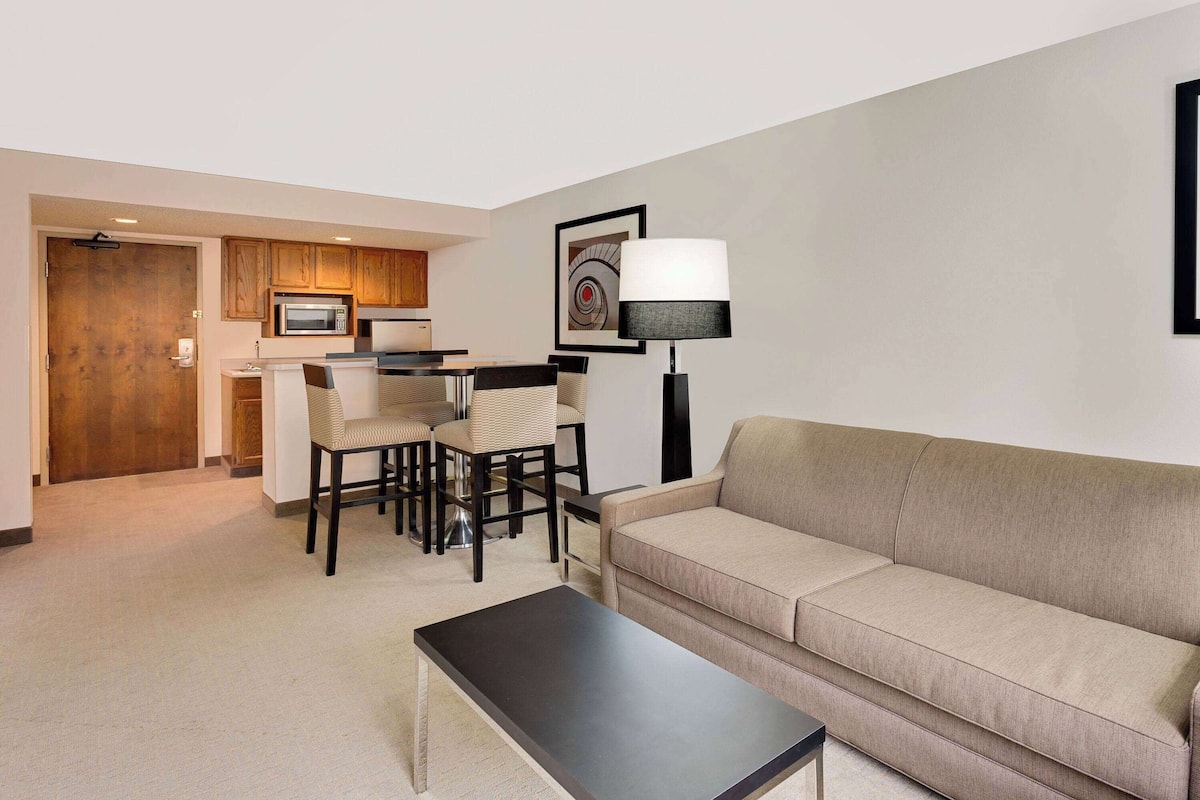 A modern living room with a beige sofa, a black coffee table, and a dining area with a table and chairs.