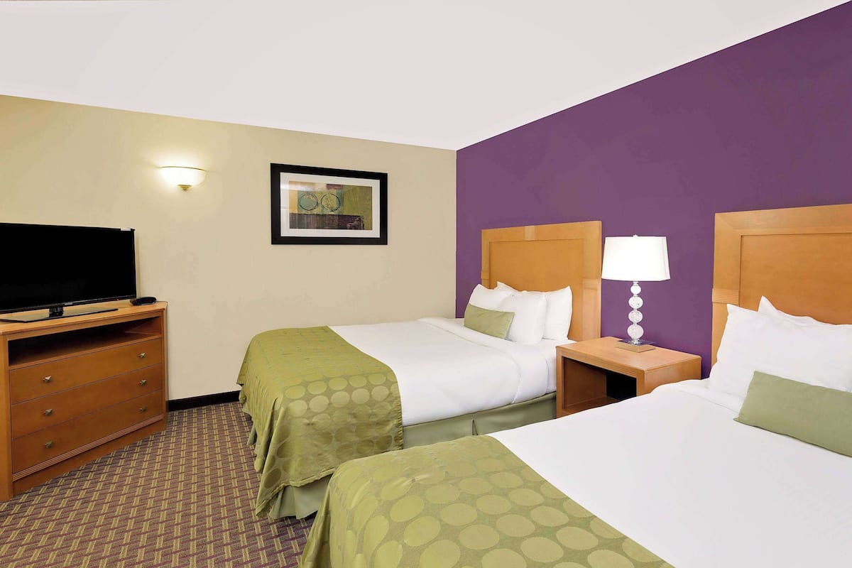 A hotel room with two beds, a TV on a wooden dresser, and a framed picture on the wall.
