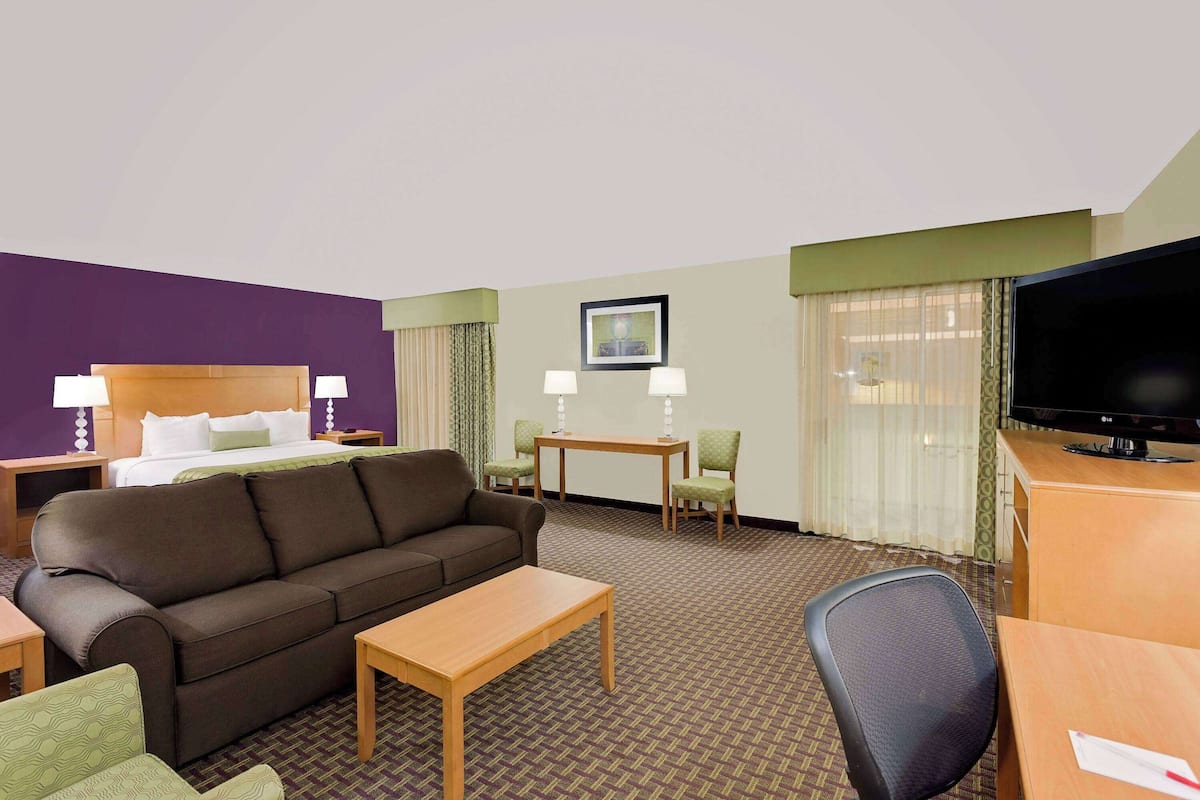 A hotel room with a bed, a sofa, a desk, a television, and two chairs.
