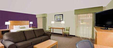 A hotel room with a bed, a sofa, a desk, a television, and two chairs.