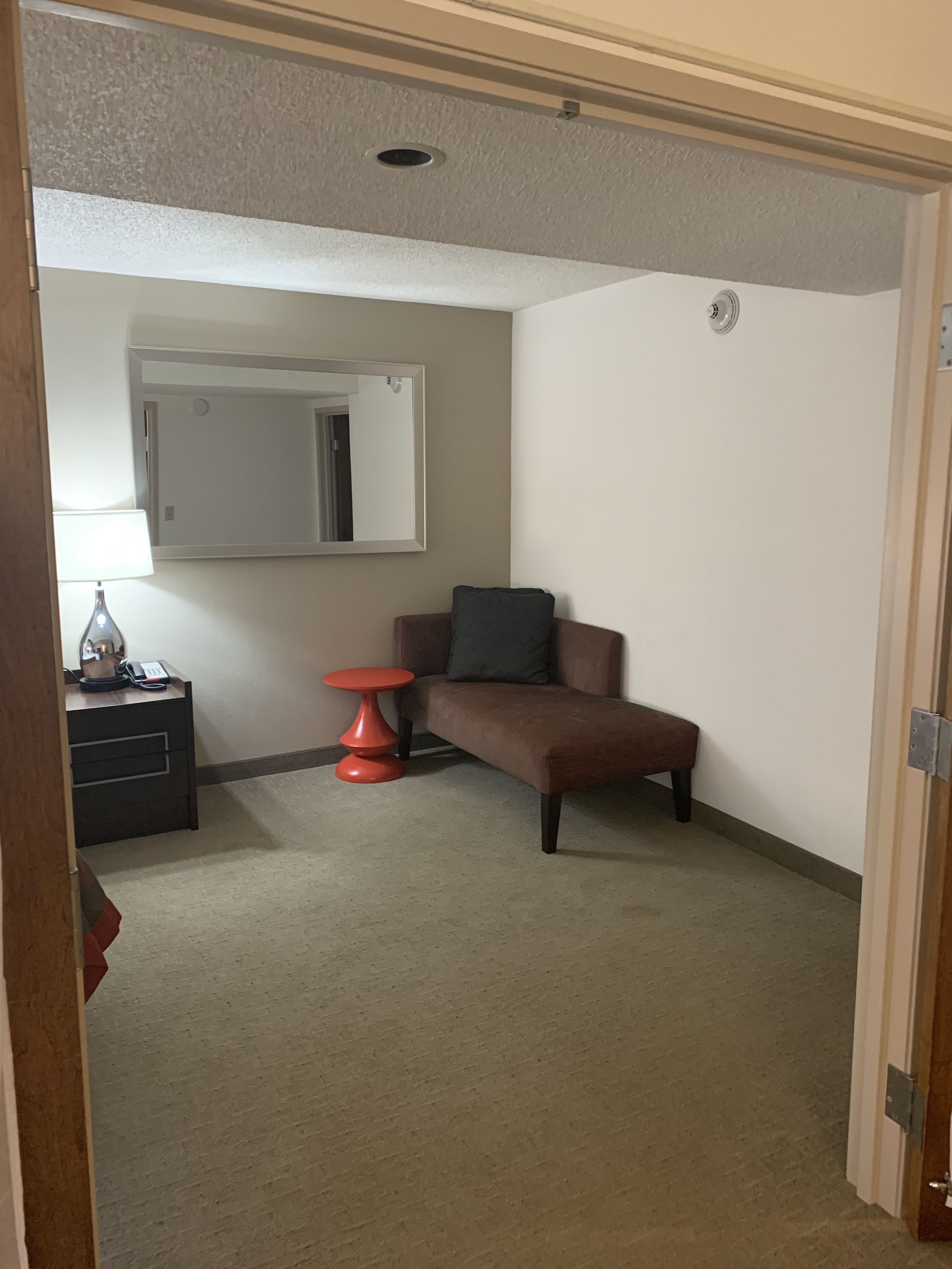 A small, sparsely furnished room with a sofa, a small table, and a mirror on the wall.