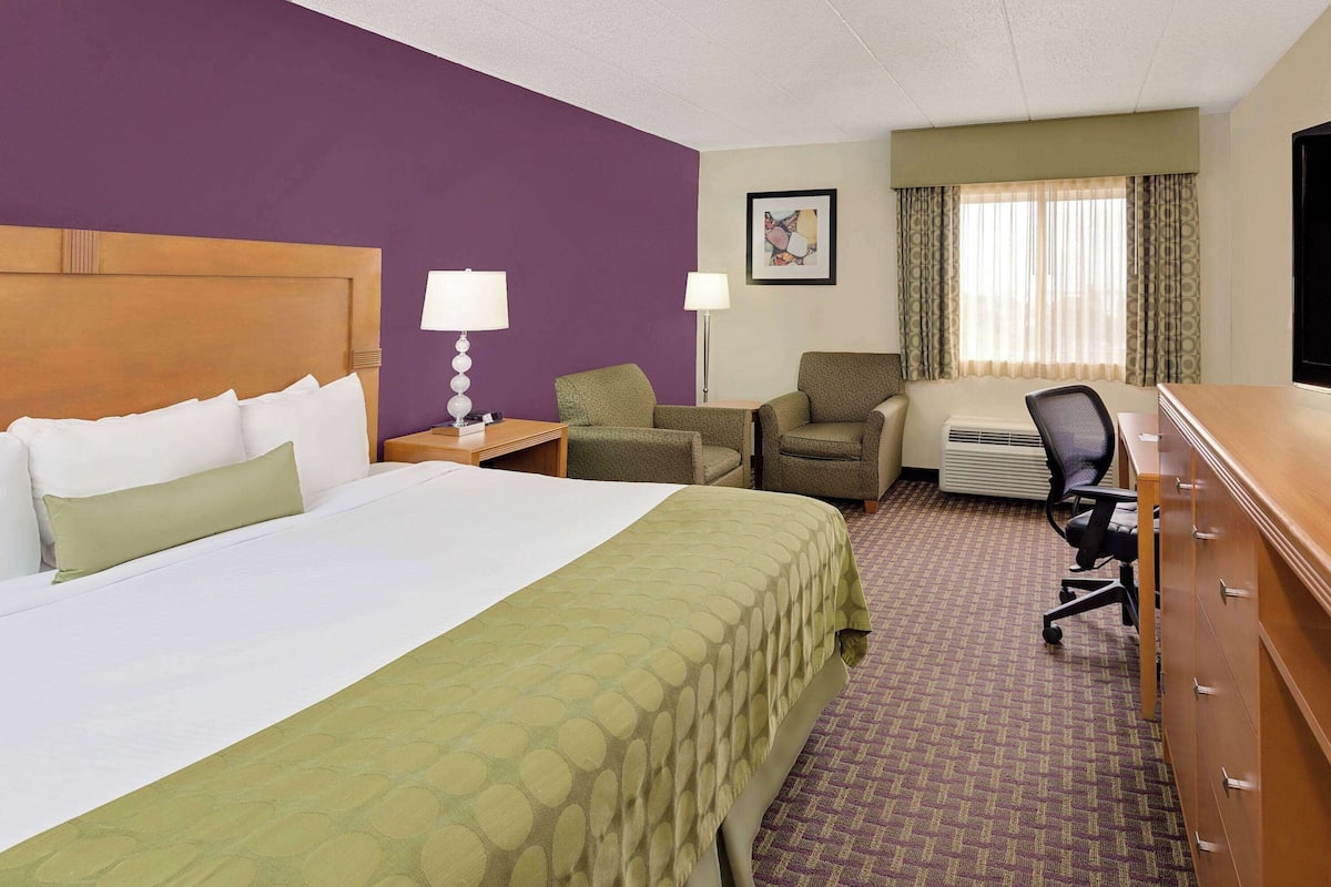 A hotel room with a bed, two chairs, a desk, a lamp, and a window with curtains.