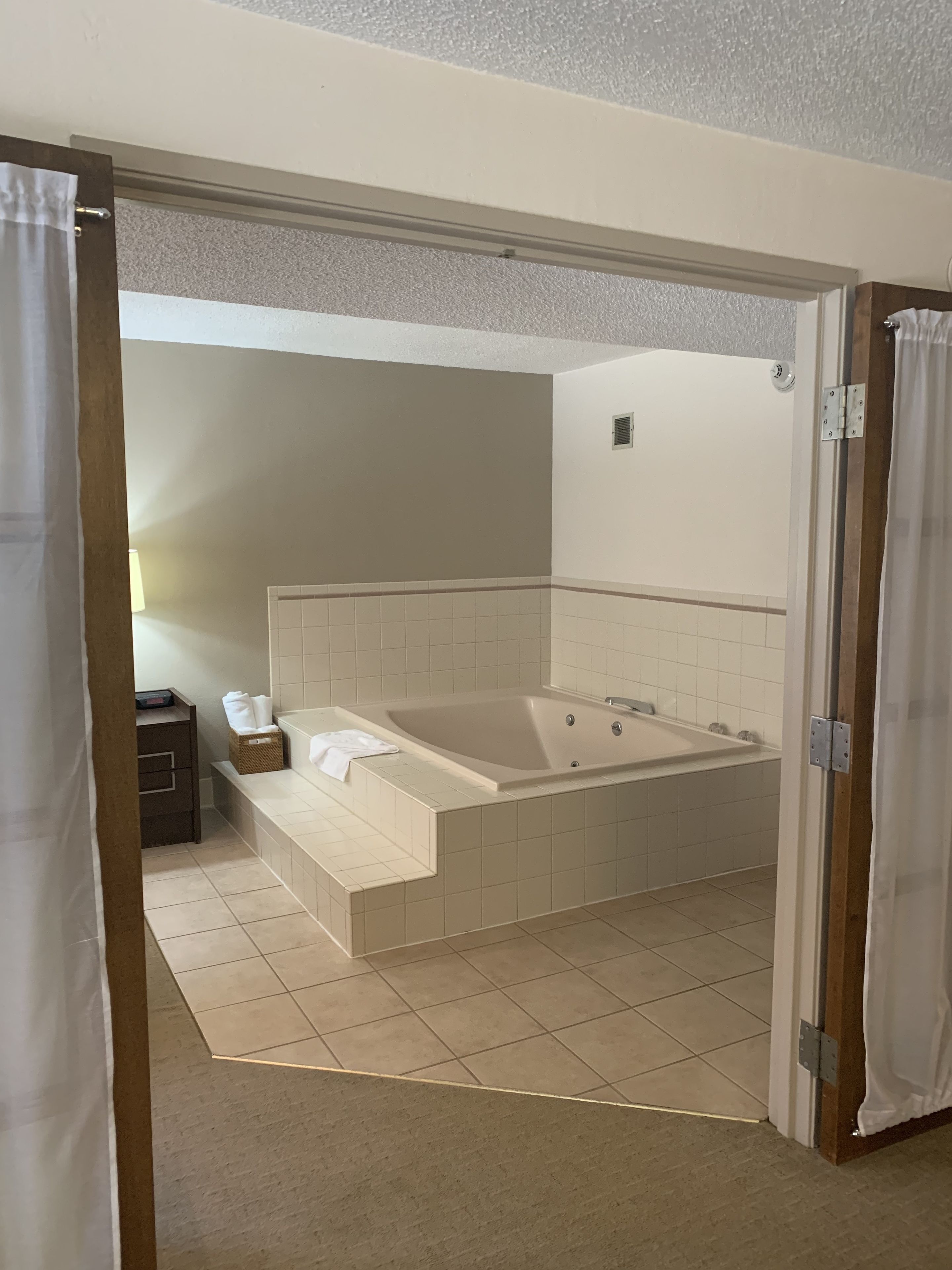 A modern bathroom with a large bathtub, a small table with a towel, and a wall-mounted heater.