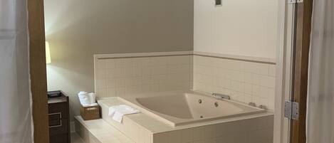 A modern bathroom with a large bathtub, a small table with a towel, and a wall-mounted heater.