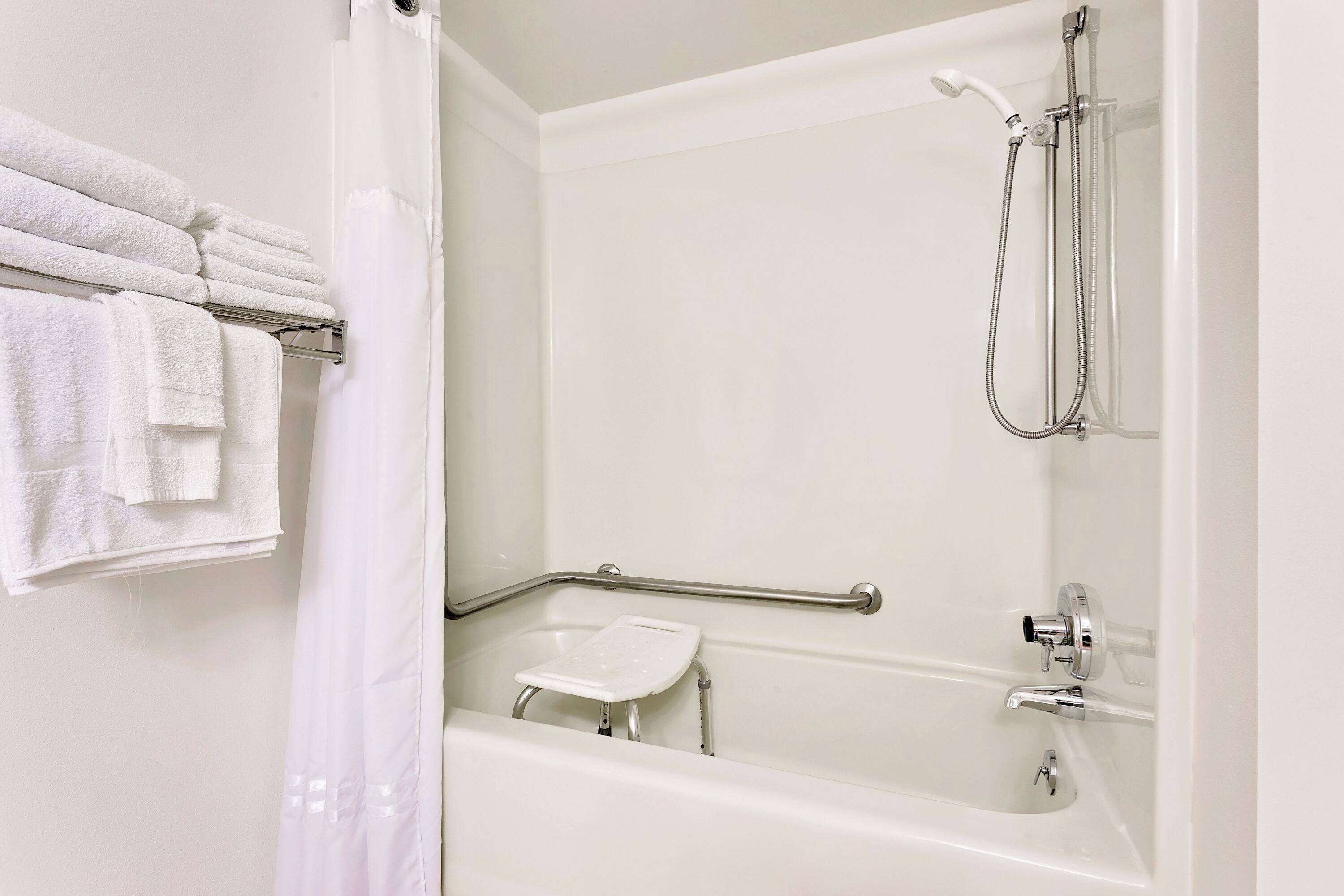 A white bathroom with a bathtub, shower, and grab bar.