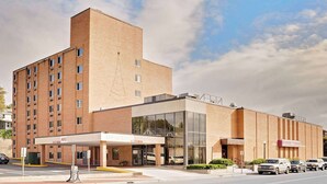 A multi-story hotel with a brick facade, a glass entrance, and a parking area.