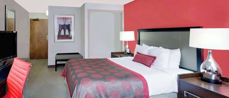 Habitación de hotel con cama, mesitas de noche, televisión, una silla roja y un cuadro en la pared.