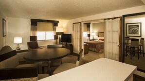 A hotel room with a dining area, a TV, a bed, and a bathroom visible through an open door.