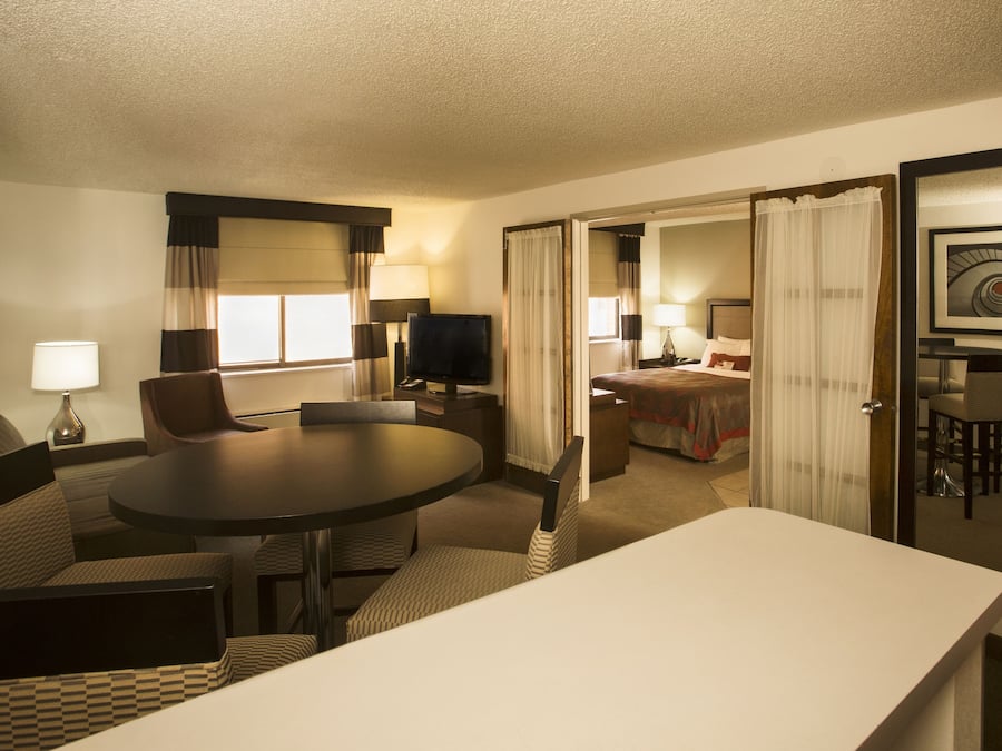 A hotel room with a dining area, a TV, a bed, and a bathroom visible through an open door.