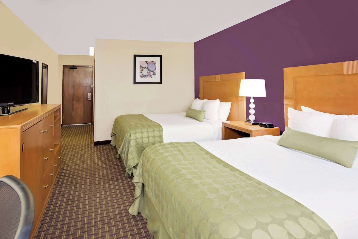 A hotel room with two beds, a television, a desk, and a door.