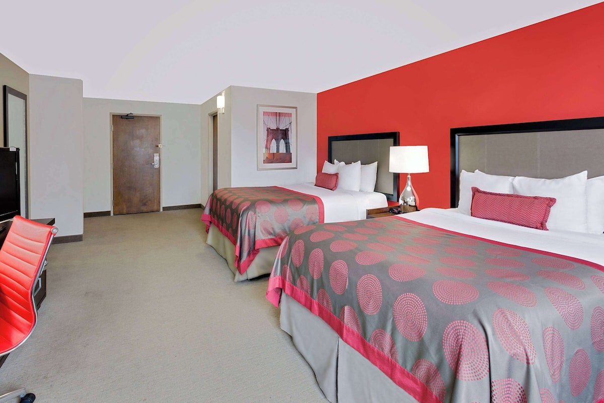 A hotel room with two beds, a red chair, a TV, and a door.
