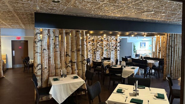 A restaurant with birch tree partitions, white tablecloths, and a ceiling with intricate designs.