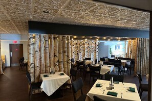 A restaurant with birch tree partitions, white tablecloths, and a ceiling with intricate designs.