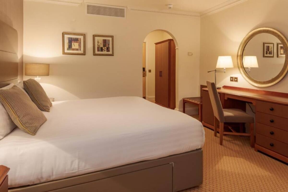 A hotel room with a bed, desk, chair, dresser, and a mirror.