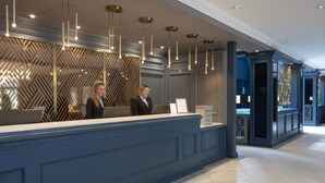 A reception desk with a modern design, featuring a blue counter and hanging pendant lights. - Belton Woods Hotel, Spa & Golf Resort (Grantham)