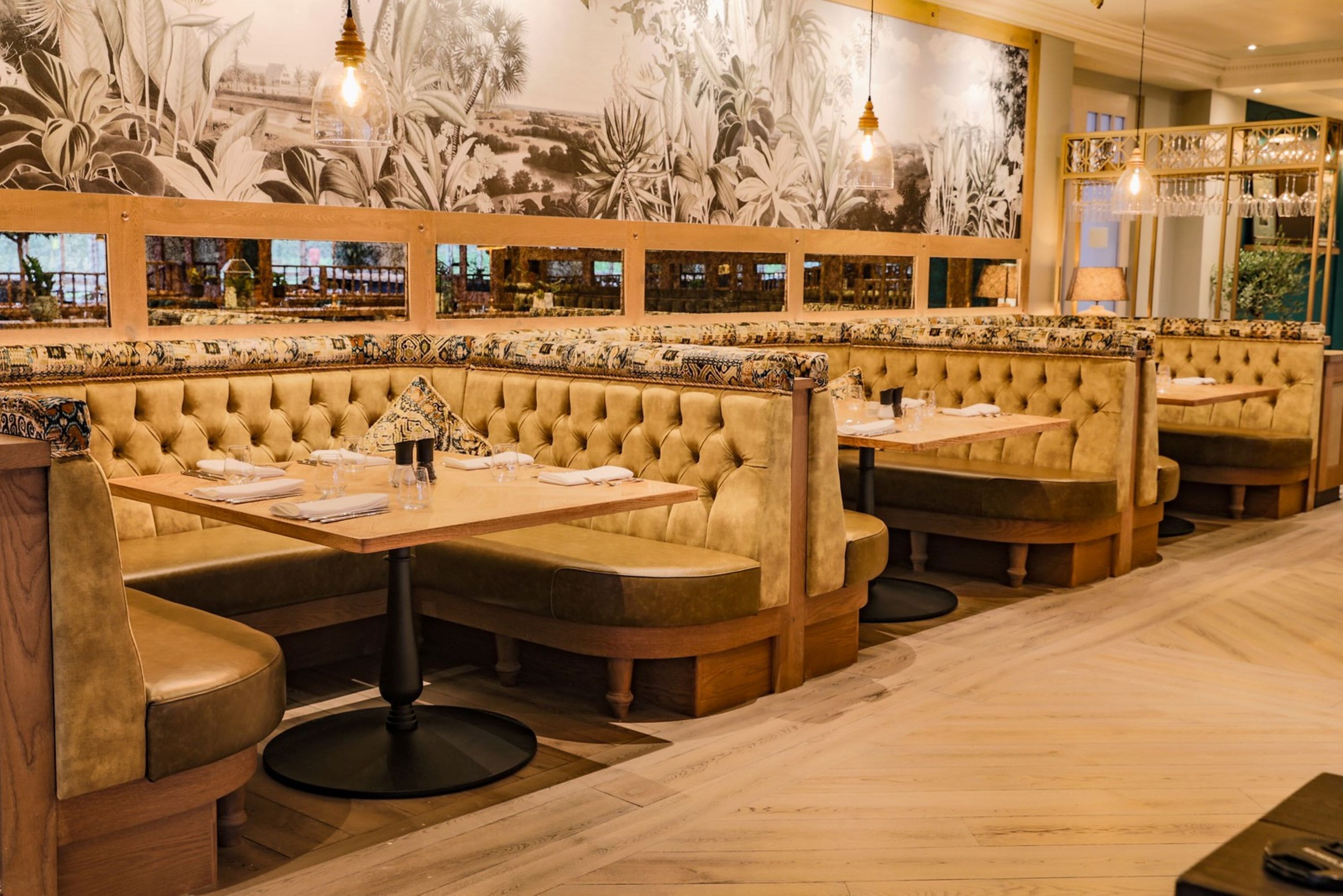 Ein Restaurant mit Sitzelementen, Holztischen und Wandgemälde.