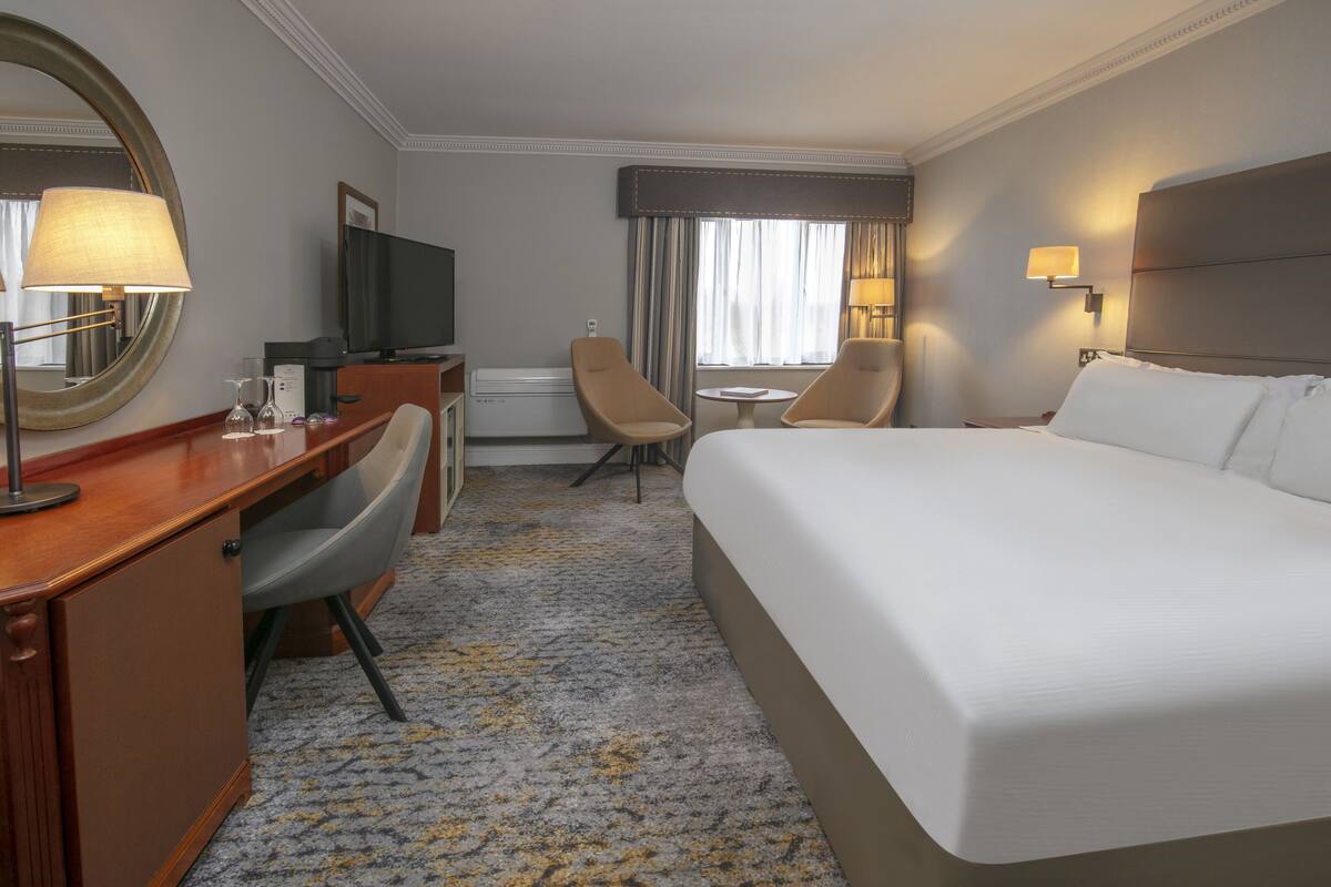 A hotel room with a large bed, a desk with a chair, a television, and a small table.